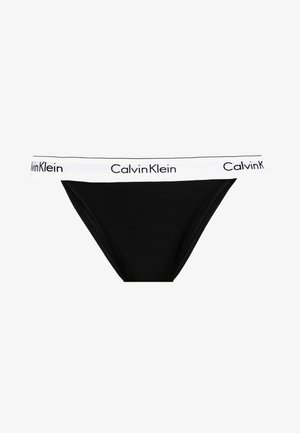 Black cotton thong with a white elastic waistband. Features the text "Calvin Klein" in black along the waistband. Smooth texture.