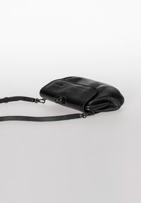 Schwarze Leder-Crossbody-Tasche mit glatter Textur, Klappenverschluss und verstellbarem Tragegurt. Sie hat eine abgerundete Form und dezente Steppnähte.