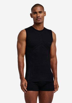 Mand iført en tætsiddende sort ærmeløs trøje og sorte boxer-shorts, stående mod en ensfarvet hvid baggrund.