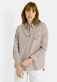 Camisa de botones a rayas en tela marrón y blanca, con un bolsillo en el pecho que tiene un diseño de perro bordado. Manga larga con botones en los puños.