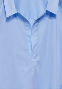 Camicia azzurro chiaro con colletto e patta a V, texture liscia e cuciture pulite. Il tessuto sembra morbido e leggero.