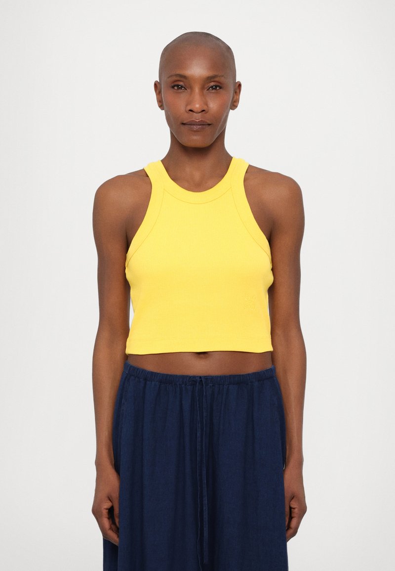 Geel geribbeld crop top met hoge hals en brede bandjes, gecombineerd met losse marineblauwe broek. Zachte textuur en aansluitend ontwerp.