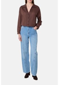Camicia button-up marrone con colletto, abbinata a jeans a vita alta a gamba larga di colore blu chiaro. Stivali alla caviglia marroni completano l'outfit.