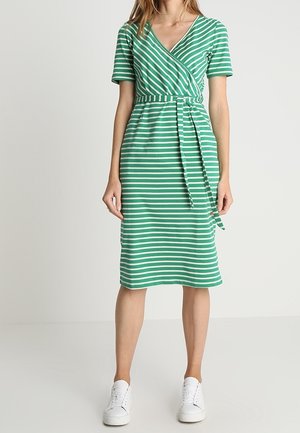 Grün-weiß gestreiftes Wickelkleid mit kurzen Ärmeln, Taillengürtel, V-Ausschnitt, knielang, kombiniert mit weißen Sneakern. Glattes Baumwollmaterial.