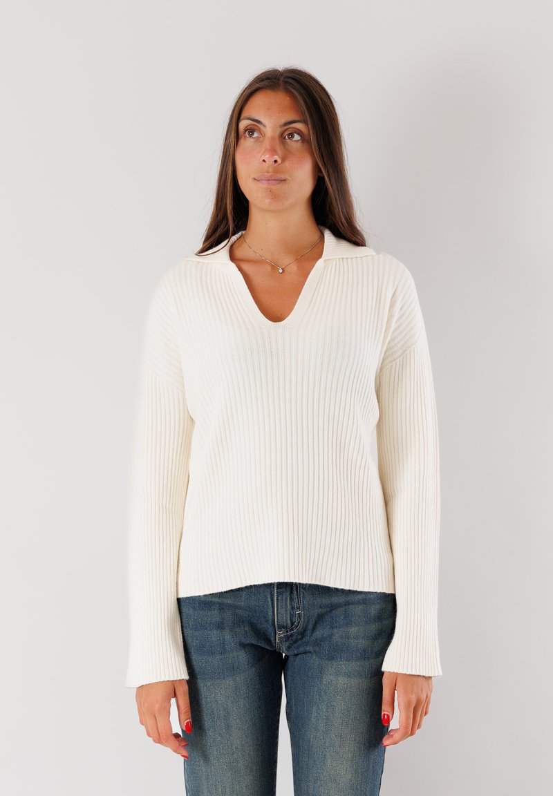 Maglione a coste di colore crema con maniche lunghe e scollatura a V, caratterizzato da una vestibilità rilassata e un tessuto testurizzato. Indossato con jeans in denim blu.