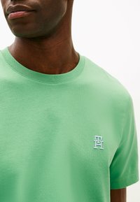 T-shirt in cotone verde con collo tondo, maniche corte e logo ricamato sul petto. Tessuto liscio e colore uniforme in tutto.