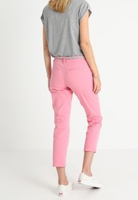 Rosa bomullsbukser med en smal, kort design. Har en klassisk midja med ett mönstrat bälte och bakfickor. Matchas med en grå skjorta.