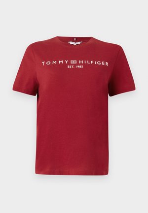 Crvena pamučna majica kratkih rukava. Sadrži bijeli tekst "TOMMY HILFIGER" i "EST. 1985" centrirano na prednjem dijelu. Glatka tekstura i okrugli izrez.