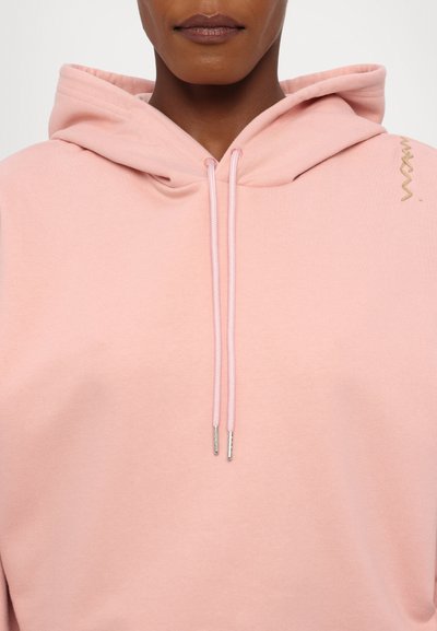 Sweatshirt capuz rosa claro com um bolso canguru, cordões ajustáveis e um pequeno detalhe em logo dourado no ombro. Material em mistura de algodão.
