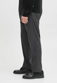 Graue, taillierte Hosen mit geradem Schnitt, aus strukturiertem Material gefertigt. Getragen mit schwarzen Lederschuhen, die ein Brogue-Design und eine flache Profilierung aufweisen.