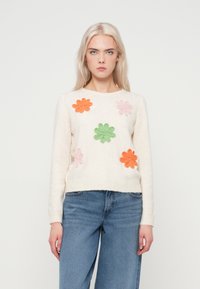 Πουλόβερ από μείγμα μαλλιού σε κρέμα, με ζωντανά κεντημένα λουλούδια σε πορτοκαλί, ροζ και πράσινο. Ριμπαριστό γιακά και μανσέτες, άνετη εφαρμογή.