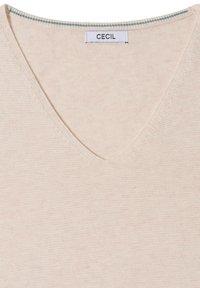 Pull en tricot beige avec un col en V et une petite étiquette blanche portant la mention "CECIL" cousue à l'intérieur du col.