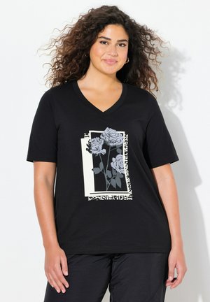 Sort v-hals t-shirt med et grafisk design af lysegrå roser inden for en hvid rektangulær ramme, sat mod en kontrasterende baggrund.