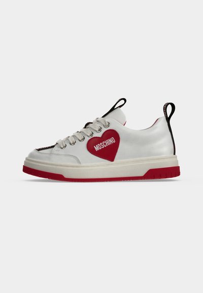 Λευκό sneaker χαμηλού τύπου με κόκκινο μπαλώμα σε σχήμα καρδιάς με την επιγραφή Moschino, λευκά κορδόνια, κόκκινη σόλα και μαύρες θηλιές στο γλώσσα και τη φτέρνα.
