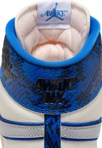 Close-up af en højtop-sneaker med et blå og sort slangeskinds-mønster, hvid indvendig polstring og "AWAKE NY" branding på hælen.