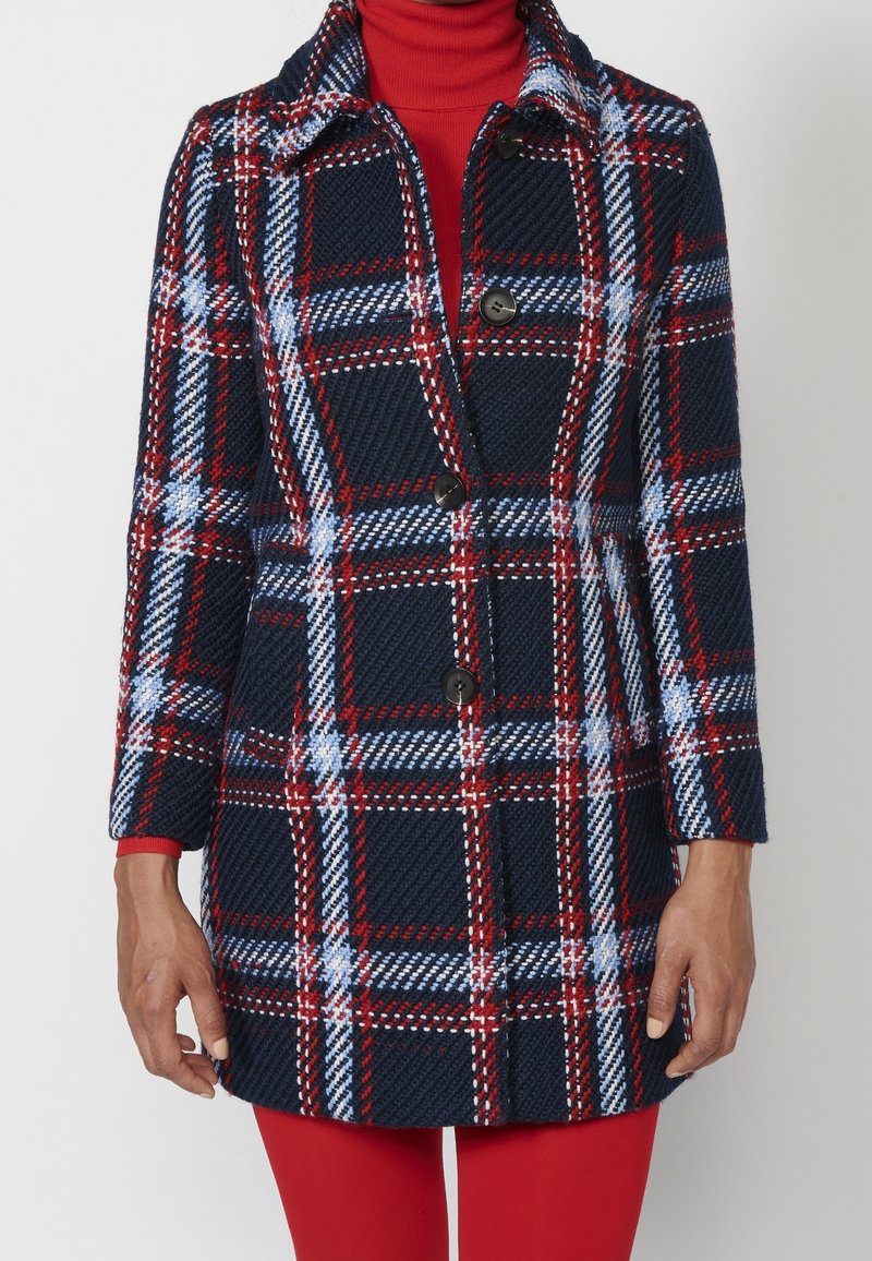Manteau en tartan marine avec motifs à carreaux rouges et blancs, fermeture à boutons et col. Texture douce avec manches longues et coupe ajustée.