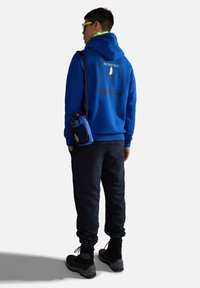 Felpa blu con grafiche nere, pantaloni scuri e stivali neri. Accompagnata da una piccola borsa blu, con tracolla e dettagli in rete.