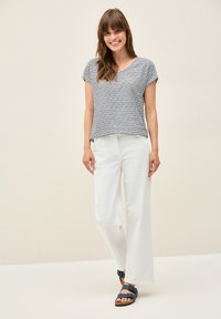 Gestreepte korte mouwen top in zwart en wit, gecombineerd met witte wijde broek en blauwe sandalen met gespaccenten.