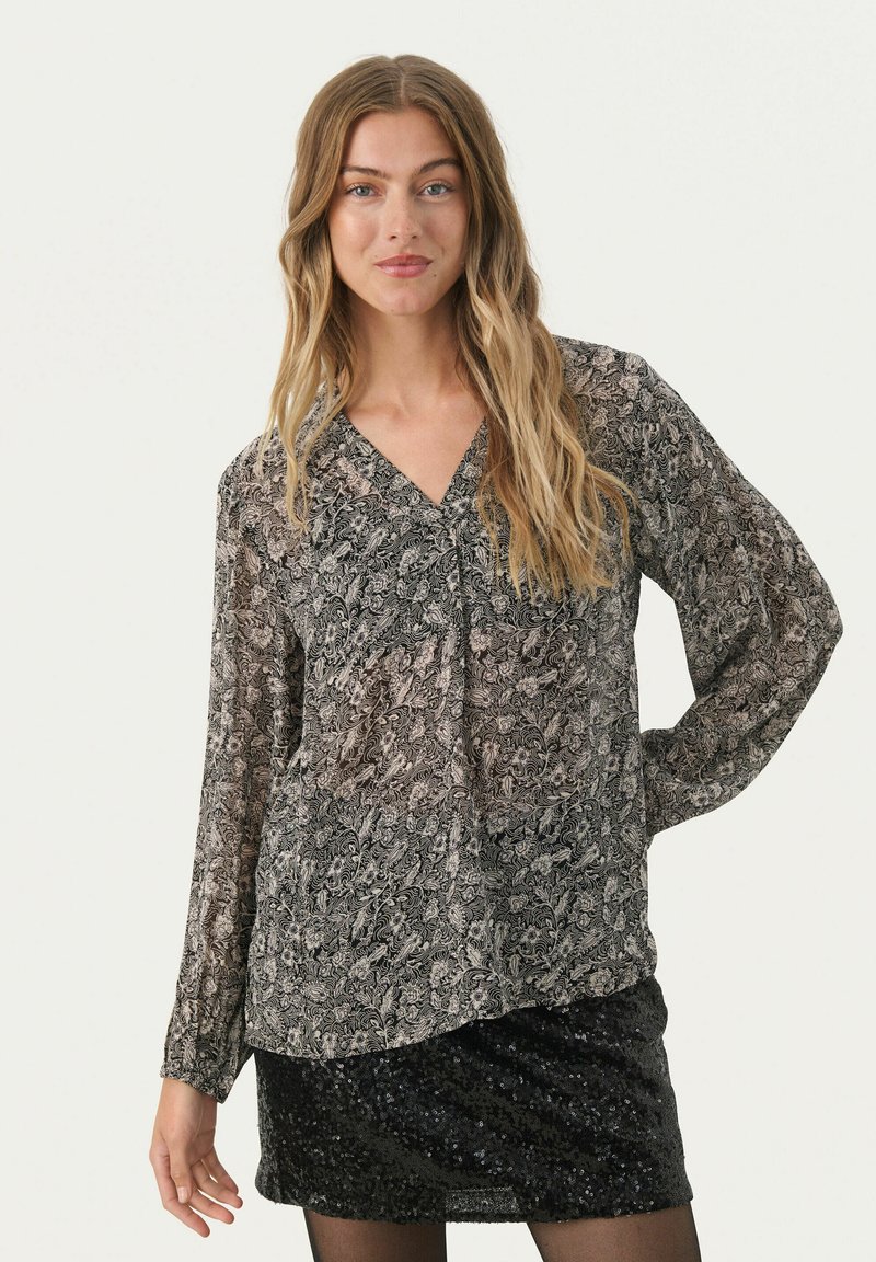 Langarmbluse mit einem schwarz-beigen Paisley-Muster, V-Ausschnitt und weichem, fließendem Stoff. Kombiniert mit einem schwarzen Paillettenrock.