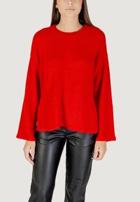 Maglione rosso oversize realizzato in un morbido tessuto peloso, con scollo rotondo e maniche ampie, abbinato a pantaloni in pelle nera.