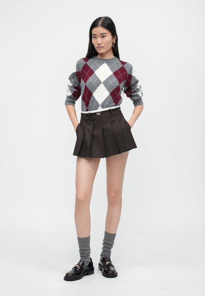 Šedý a burgundský argyle sveter, plisovaná hnedá sukňa, šedé ponožky a čierne topánky s lesklým povrchom. Súprava má štruktúrovanú siluetu.