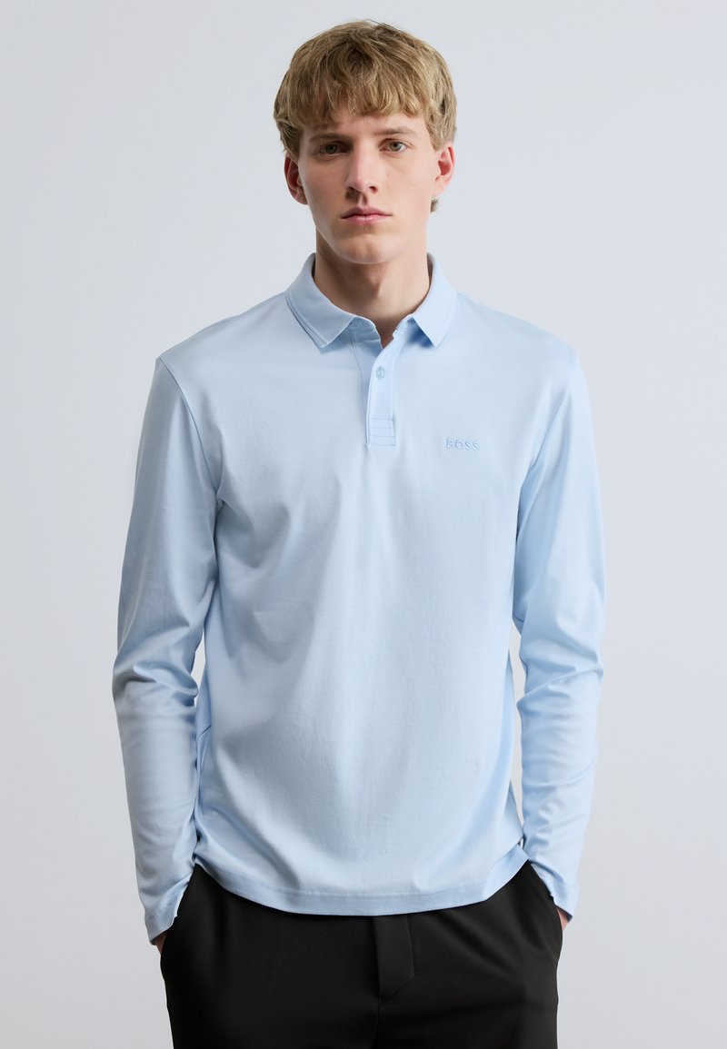 Φωτεινό γαλάζιο μπλουζάκι πόλο με μακριά μανίκια και κλειστό γιακά, με διακριτική κεντημένη λογότυπο στο αριστερό στήθος. Λείο ύφασμα και εφαρμοστό σχέδιο.