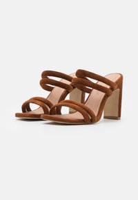 Bruine suede hoge hakken sandaal met twee brede banden aan de voorkant en een dikke hak. De binnenzool heeft een lichte natuurlijke kleur.