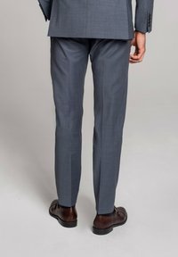 Szary garnitur biznesowy w delikatną prążkowaną wzór, dopasowany krój. Widoczne ciemno brązowe skórzane buty, z subtelnymi detalami na sznurówkach.