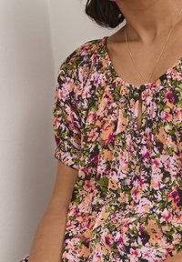 Blommig blus i rosa, orange och grönt. Korta puffärmar, rundad hals med nyckelhåls- och knapppunkt. Lätt, texturerad tyg.