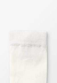 Hvit bomullssokk med ribbet topp, jevn tekstur og et enkelt design. Sokken har en middels tykkelse og er uten mønstre eller farger.
