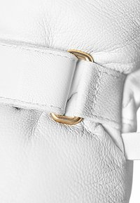 Weißes Leder mit strukturierter Oberfläche, ausgestattet mit einem goldenen Hardware-Loop und einem genähten Riemendetail.