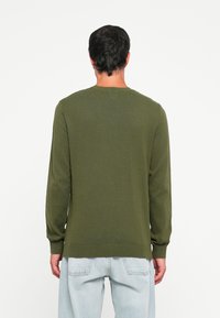 Groene gebreide trui met lange mouwen en geribde manchetten, met een ronde halslijn en een ontspannen pasvorm, gecombineerd met lichtblauwe denim jeans.