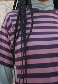 Lilla og pink stribet t-shirt med korte ærmer, blødt stof og rundt udskæring, lagd på en lys blå turtleneck.