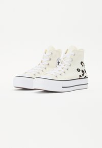Höga canvas sneakers i krämfärg med vita snören, svarta detaljer och leopardfläckar på sidan. Har en gummisula och rund tå.