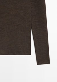 Brun striktrøje med lange ærmer og fin ribstruktur vist mod hvid baggrund, hvor detaljer på ærmer og bundkant fremhæves.