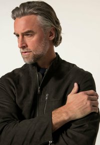 Chaqueta de ante negra con cierre frontal, cuello alto y dos bolsillos con cremallera. La tela tiene una textura suave y un acabado mate.