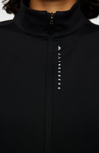 Sort zip-up jakke lavet af glat materiale, med høj krave, fuldlængde lynlås og hvid logo-tekst langs lynlåslinjen.