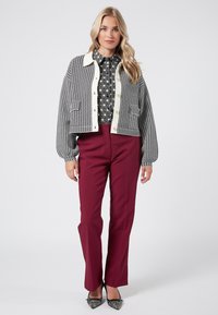 Vävt svart och vitt kortjacka med knappstängning och texturerade fickor, i kombination med vinröda figursydda byxor och mönstrad blus.