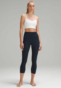 Vit croppad topp med tunna axelband och marinblå högmidjade leggings, båda tillverkade av slätt, stretchigt tyg. Rent design, inga synliga mönster.