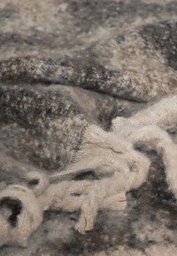 Uldeppe med en blanding af grå og brune nuancer, der har en blød, tekstureret overflade og cremefarvede frynser.
