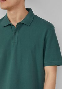 Kurzärmliges Poloshirt aus dunkelgrünem Baumwollstoff mit strukturierter Oberfläche. Ausgestattet mit einem klassischen Kragen und einer Knopfleiste mit drei Knöpfen. Dezentes Logo-Detail.