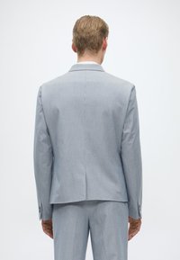 Γκρι κοστούμι τύπου σακάκι με μονό άνοιγμα, εφαρμοστό και με διακριτό ρίγες. Διαθέτει καπάκι λαιμού και κουμπωμένα μανίκια.