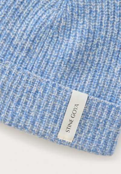 Bonnet en laine tricotée bleu clair et blanc avec une texture côtelée et une étiquette rectangulaire blanche portant l’inscription "STINE GOYA" cousue près du bord.