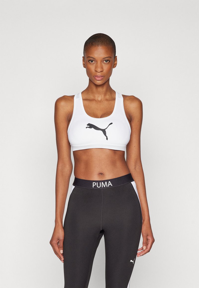 Hvit sport-bh med svart Puma-logo, med brede stropper og glatt stoff. Kombinert med svarte leggings som har "PUMA" på midjen.
