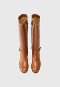 Botas marrones de cuero hasta la rodilla con un acabado liso, que cuentan con cremalleras y correas decorativas, expuestas sobre un fondo blanco liso.
