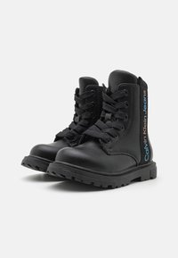 Czarne sznurowane botki wykonane z syntetycznej skóry, z grubą gumową podeszwą i logo "Calvin Klein Jeans" w niebieskim i czerwonym kolorze po boku.