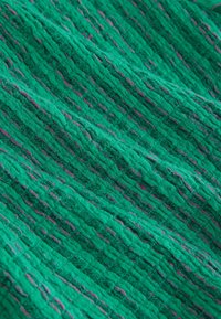 Tissu tricoté vert avec un motif côtelé et texturé, parsemé de fines taches violettes.