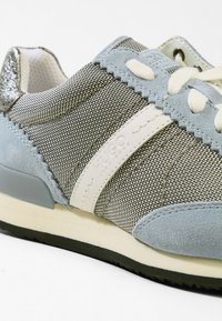 Gros plan sur une sneaker grise et bleu clair avec des lacets blancs, un tissu texturé, des détails en daim et la marque "HUGO" sur la bande latérale.