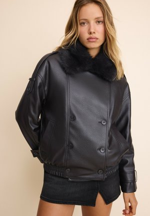 Jeune femme portant une veste en cuir noire texturée avec un grand col en fourrure et une mini-jupe noire sur un fond beige uni.