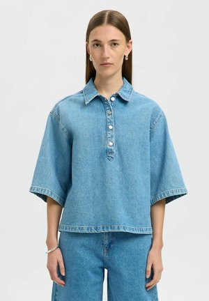 Top in denim azzurro chiaro con colletto, maniche corte e ampie, e chiusura con bottoni. Presenta una vestibilità rilassata e dettagli di cucitura visibili.